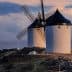 Two traditional windmills with black blades and white stone structures situated on a hilltop. - Olive Oil Times