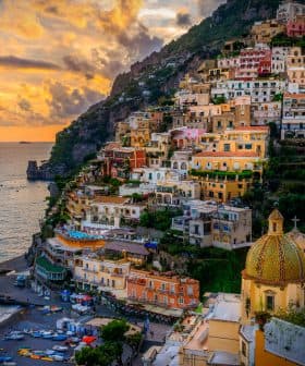 View of the coastal town of Positano with colorful buildings and a beach during sunset. - Olive Oil Times