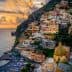 View of the coastal town of Positano with colorful buildings and a beach during sunset. - Olive Oil Times