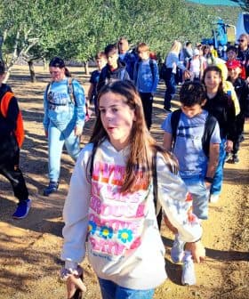 A group of students walking in an olive grove, wearing backpacks and casual clothing. - Olive Oil Times