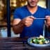 Individual holding a smartphone to take a photo of a salad dish on a wooden table. - Olive Oil Times