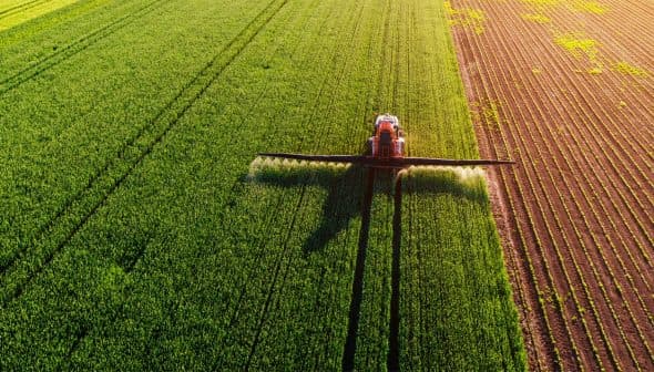 Aerial view of an agricultural sprayer applying treatment to a green field. - Olive Oil Times