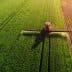 Aerial view of an agricultural sprayer applying treatment to a green field. - Olive Oil Times