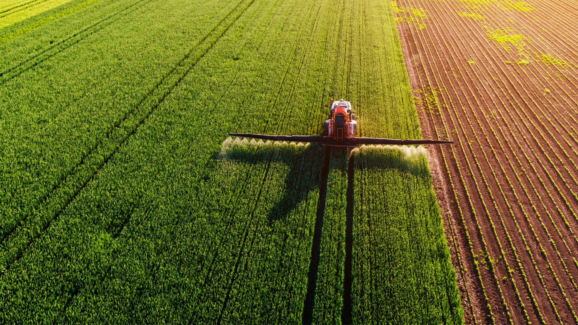 Aerial view of an agricultural sprayer applying treatment to a green field. - Olive Oil Times