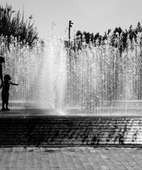Silhouettes of children playing in a water fountain with water spraying in the background. - Olive Oil Times