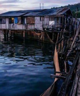 Wooden stilt houses built over water with a wooden walkway leading to them during twilight. - Olive Oil Times