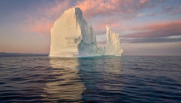 A large iceberg floating in calm water with a colorful sky at sunset. - Olive Oil Times