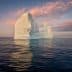 A large iceberg floating in calm water with a colorful sky at sunset. - Olive Oil Times