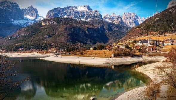 Scenic view of a lake reflecting mountains and a village in the foreground. - Olive Oil Times
