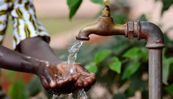 A person washing hands under a flowing tap with water in an outdoor setting. - Olive Oil Times