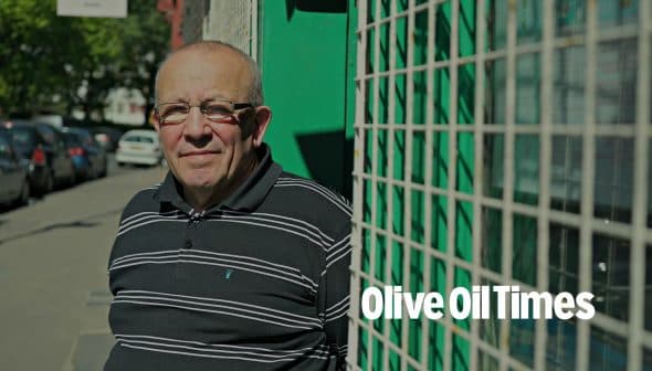 Man wearing glasses and a striped shirt standing next to a green fence with a grid pattern. - Olive Oil Times