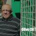 Man wearing glasses and a striped shirt standing next to a green fence with a grid pattern. - Olive Oil Times