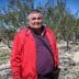 Man wearing a red jacket and purple shirt standing in an olive grove with trees in the background. - Olive Oil Times
