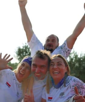 Four individuals celebrating outdoors with expressions of joy and excitement, two in the foreground and two in the background. - Olive Oil Times