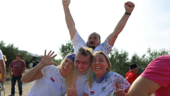 Four individuals celebrating outdoors with expressions of joy and excitement, two in the foreground and two in the background. - Olive Oil Times