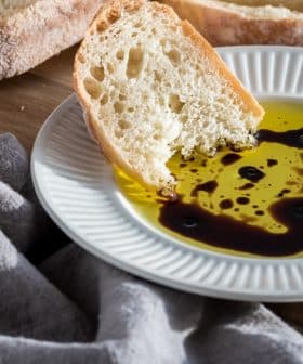 Slice of bread dipped in olive oil with balsamic vinegar on a white plate. - Olive Oil Times