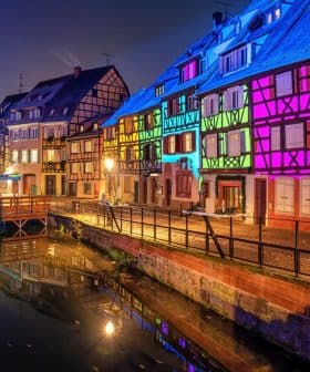 Row of half-timbered houses illuminated in various colors along a canal at night. - Olive Oil Times
