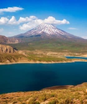 Snow-capped mountain with a clear blue sky above a large lake surrounded by hills. - Olive Oil Times