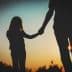 Silhouette of an adult and a child holding hands against a sunset background. - Olive Oil Times