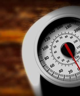 Analog weight scale featuring a round dial with a red pointer and numerical markings. - Olive Oil Times