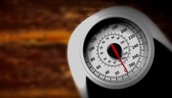 Analog weight scale featuring a round dial with a red pointer and numerical markings. - Olive Oil Times