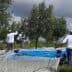 Workers using equipment to harvest olives from trees while standing on a blue tarp. - Olive Oil Times