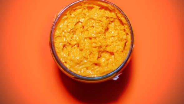 Glass jar filled with orange condiment on a bright orange background. - Olive Oil Times