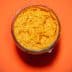 Glass jar filled with orange condiment on a bright orange background. - Olive Oil Times