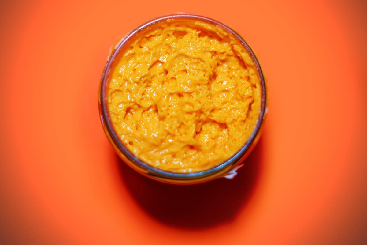 Glass jar filled with orange condiment on a bright orange background. - Olive Oil Times