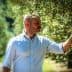 Man in a light shirt examining an olive tree branch in a natural setting. - Olive Oil Times