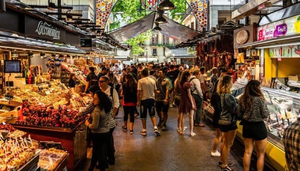 A busy market scene with numerous stalls selling a variety of goods and many people browsing. - Olive Oil Times