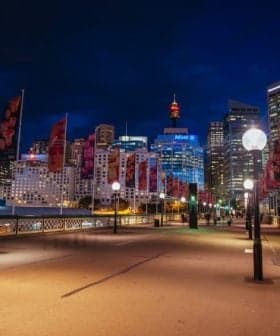 Night view of Sydney cityscape featuring illuminated buildings and decorative flags along a walkway. - Olive Oil Times