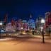 Night view of Sydney cityscape featuring illuminated buildings and decorative flags along a walkway. - Olive Oil Times