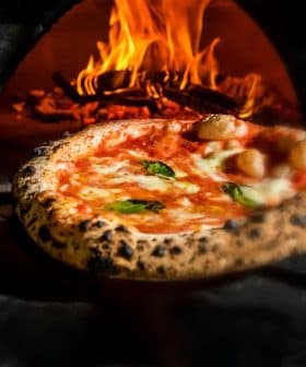 A freshly baked pizza with melted cheese and basil being pulled from a wood-fired oven. - Olive Oil Times