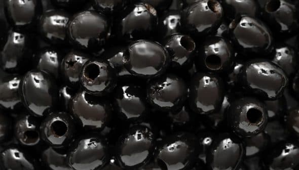 Close-up image of shiny black olives with visible holes. - Olive Oil Times