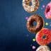Four assorted donuts with chocolate, pink, and white icing, topped with sprinkles and colorful decorations. - Olive Oil Times