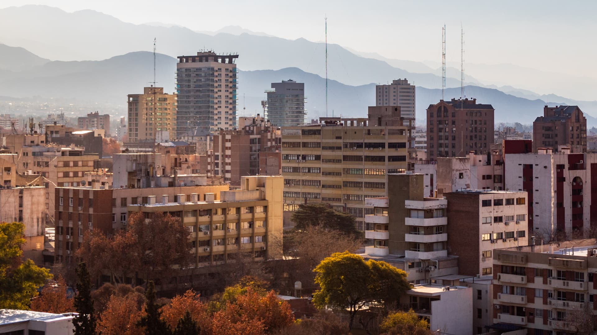 A cityscape featuring various buildings with mountains visible in the background under a clear sky. - Olive Oil Times