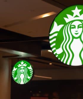 Illuminated Starbucks logo sign featuring a green background and white mermaid design. - Olive Oil Times