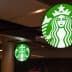 Illuminated Starbucks logo sign featuring a green background and white mermaid design. - Olive Oil Times