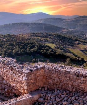 Stone ruins overlooking a mountainous landscape during sunset with a colorful sky. - Olive Oil Times