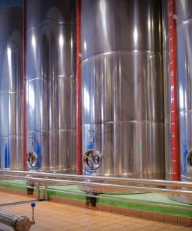 Row of stainless steel fermentation tanks used in winemaking process inside a winery. - Olive Oil Times