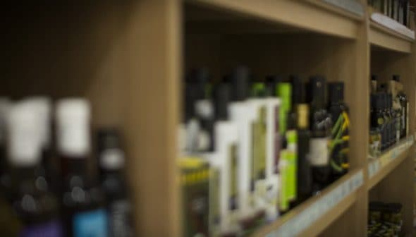 Various bottles of olive oil displayed on wooden shelves in a store. - Olive Oil Times