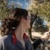 Woman with a ponytail holding a stick while harvesting olives from a tree. - Olive Oil Times