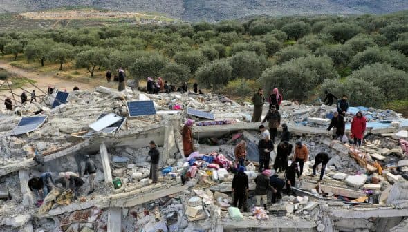 People searching through the rubble of a collapsed building surrounded by olive trees. - Olive Oil Times