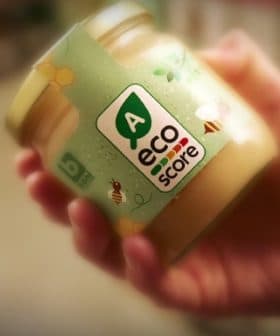 Hand holding a jar labeled with an eco score rating and a green logo. - Olive Oil Times