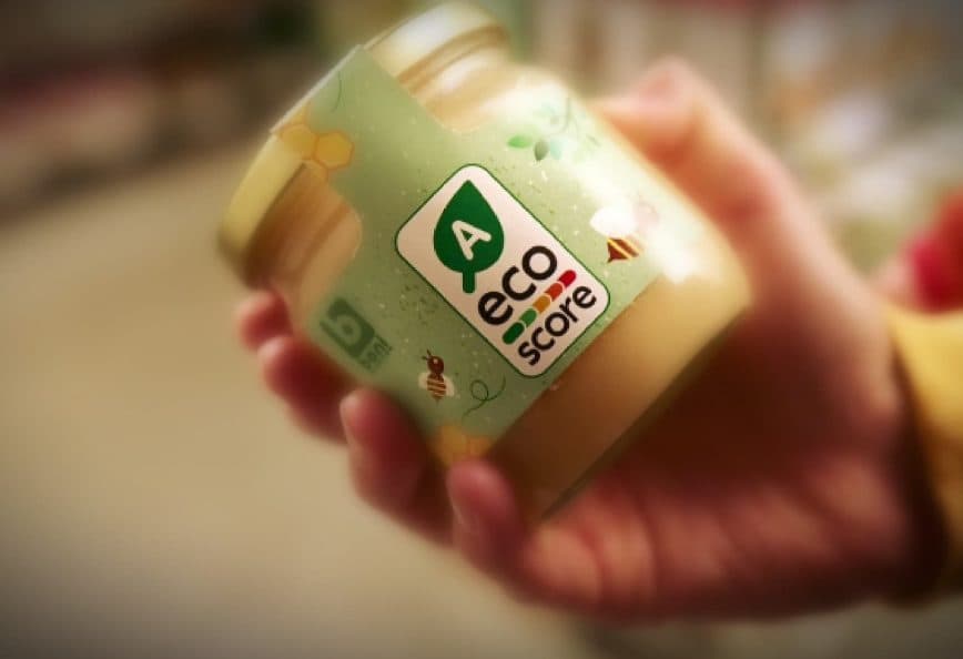 Hand holding a jar labeled with an eco score rating and a green logo. - Olive Oil Times