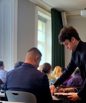 A young man serving food to a seated participant during a presentation on olfactory sensations. - Olive Oil Times