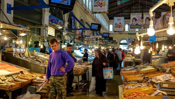 Interior view of a fish market with customers browsing and vendors displaying seafood. - Olive Oil Times