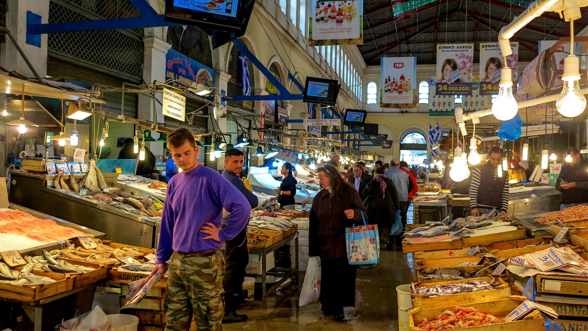 Interior view of a fish market with customers browsing and vendors displaying seafood. - Olive Oil Times