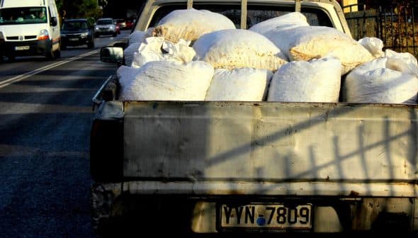 Pickup truck with a bed full of white bags on a street. - Olive Oil Times